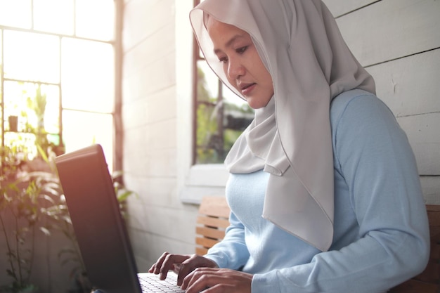 Mujer musulmana asiática sonriendo escribiendo en una computadora portátil empresaria exitosa que trabaja en casa