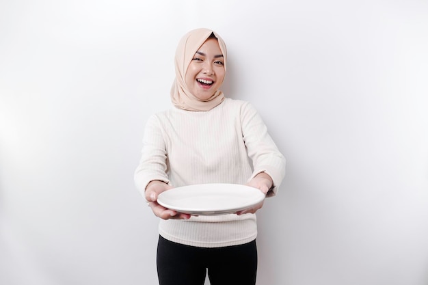 Una mujer musulmana asiática sonriente está ayunando y hambrienta y sosteniendo y señalando un plato