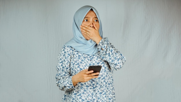 Mujer musulmana asiática sorprendida que sostiene un teléfono inteligente