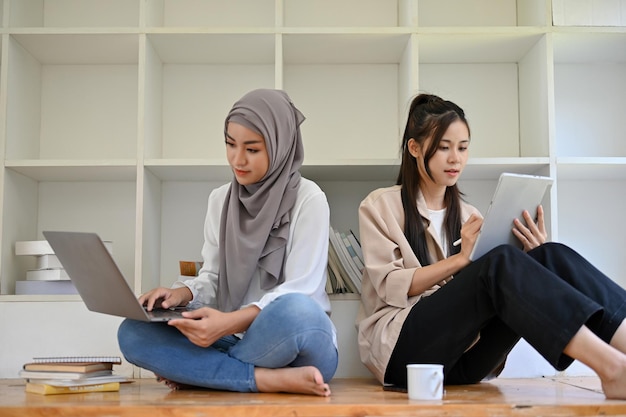 Mujer musulmana asiática y su amiga se concentraron usando su computadora portátil y tableta