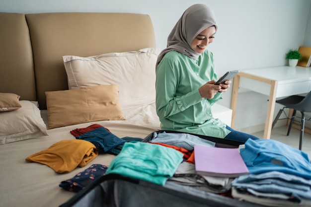 Mujer musulmana asiática utilizando su teléfono móvil con maleta llena