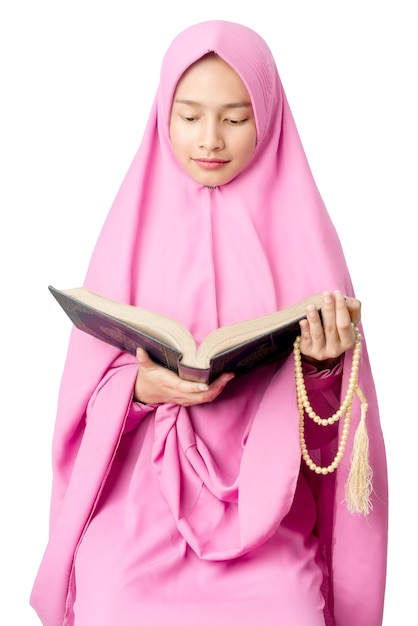 Mujer musulmana asiática en un velo con cuentas de oración y leyendo el Corán