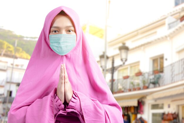 Mujer musulmana asiática en un velo y con máscara de gripe rezando