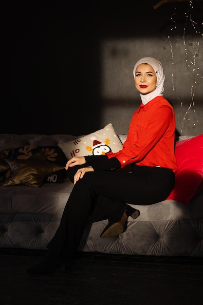 Mujer musulmana cerca de luces de Navidad y decoración en estudio. Modelo musulmán profesional posando en la víspera de año nuevo