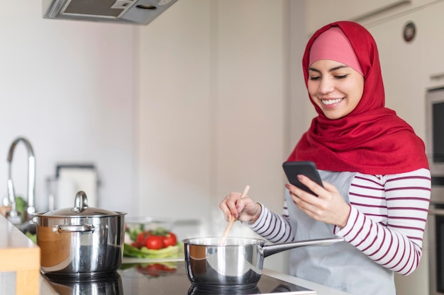 Mujer musulmana cocinando en casa leyendo un blog culinario en un smartphone