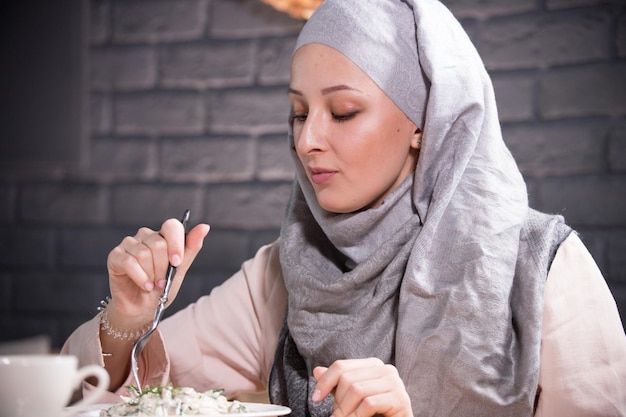 Mujer musulmana come con un tenedor en un café