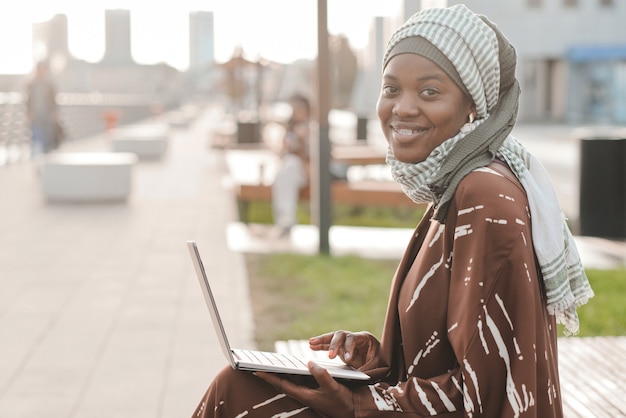 Mujer musulmana escribiendo en el portátil al aire libre