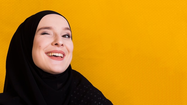 Foto mujer musulmana feliz parpadeando ojos sobre fondo amarillo