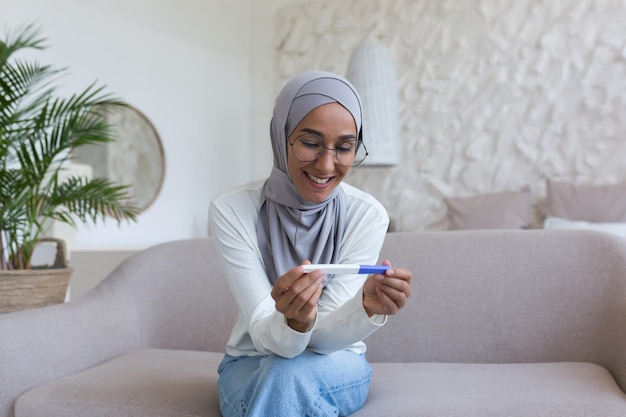 Mujer musulmana feliz y sonriente en hijab con prueba de embarazo en casa mujer árabe feliz con el resultado