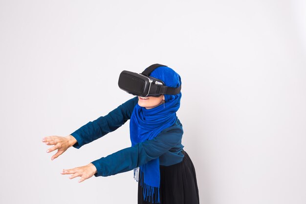 Mujer musulmana con gafas de realidad virtual. Foto de estudio, fondo blanco.