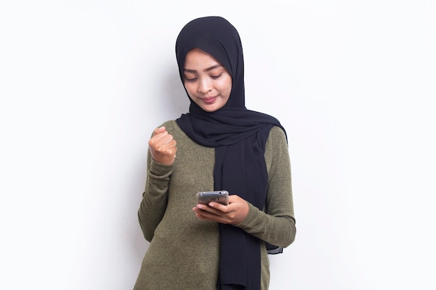 Mujer musulmana hermosa asiática joven feliz que usa el teléfono móvil aislado en el fondo blanco