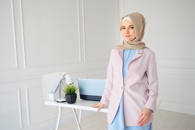 Mujer musulmana en hijab beige y ropa tradicional de pie cerca del lugar de trabajo