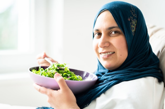 Foto mujer musulmana con hijab comiendo su ensalada verde sola