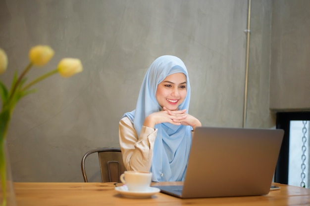 Mujer musulmana con hijab está trabajando con una computadora portátil en la cafetería.