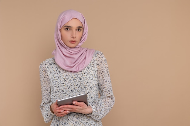 Mujer musulmana joven y bonita en hijab digital con una tableta en las manos