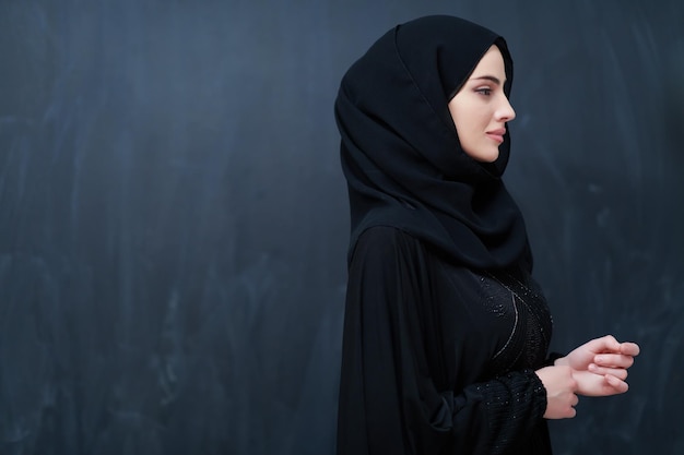 Mujer musulmana joven moderna en abaya negra. Niña árabe con ropa tradicional y posando frente a una pizarra negra. Representando el estilo de vida árabe moderno y rico