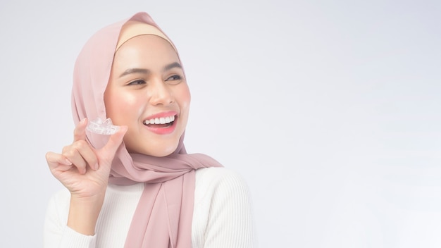 Una mujer musulmana joven que sostiene los apoyos invisalign sobre el estudio del fondo blanco, la salud dental y el concepto de la ortodoncia.