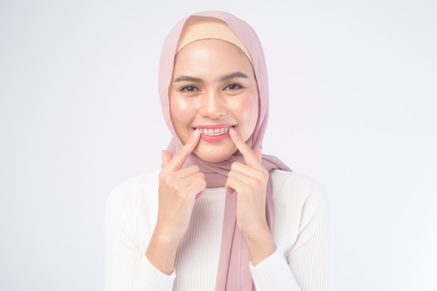 Una mujer musulmana joven que sostiene el retenedor colorido para los dientes sobre el estudio del fondo blanco, la salud dental y el concepto de ortodoncia.