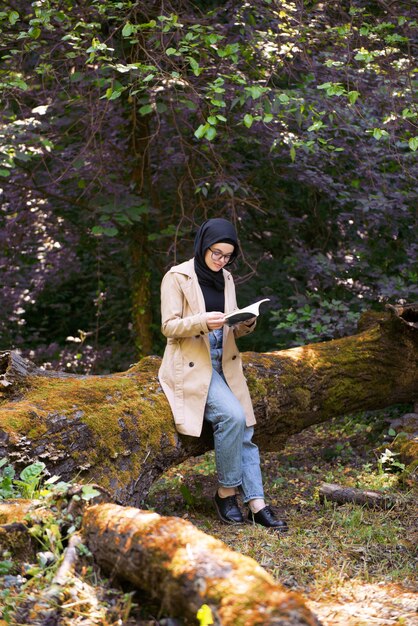 Mujer musulmana leyendo un libro en el parque durante su tiempo libre.