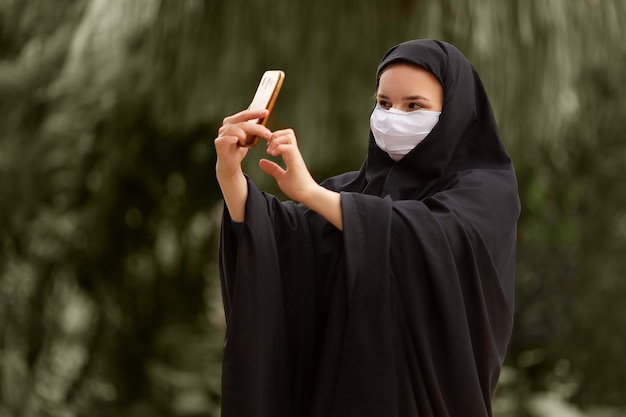 Mujer musulmana con máscara quirúrgica tomando una selfie con su teléfono inteligente Covid19 Coronavirus