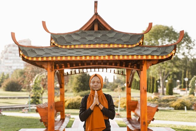 Mujer musulmana negra meditando qigong cerca del cenador chino. Mujer africana hace entrenamiento deportivo chino al aire libre.