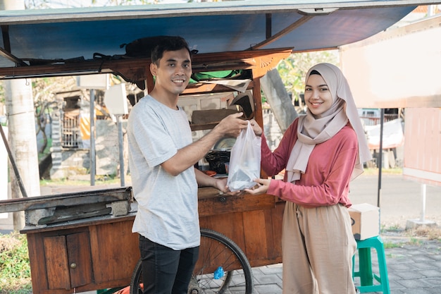 Mujer musulmana pidiendo satay de pollo a un vendedor de carritos de comida pequeños