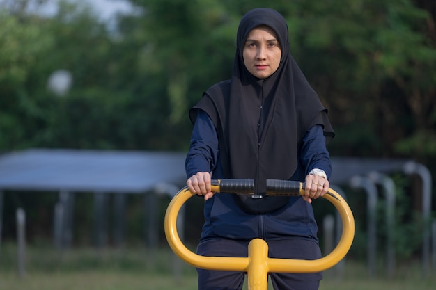 Mujer musulmana con ropa oscura y hijab cubre sus ejercicios de cabello en el parque.