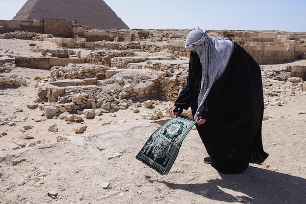 Mujer musulmana con ropa de túnica preparándose para rezar en el desierto