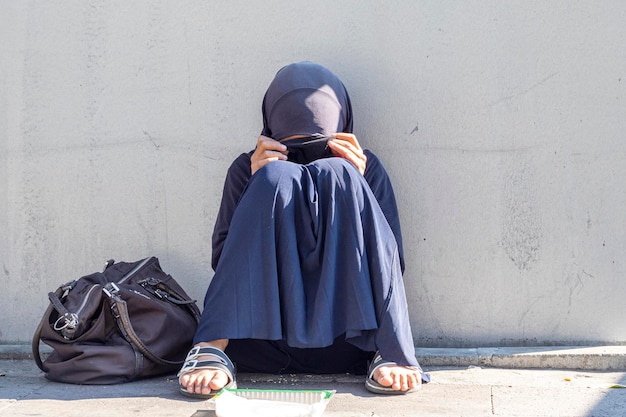 Mujer musulmana sentada en una calle de la ciudad Mujer musulmana con la cara cerrada pidiendo limosna