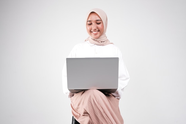 Foto una mujer musulmana está sentada en una silla y está usando una computadora portátil