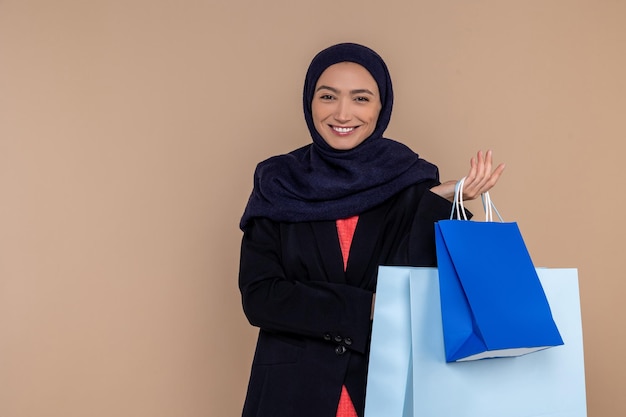 Mujer musulmana sonriente en hijab de pie con bolsas de compras aisladas sobre un fondo beige