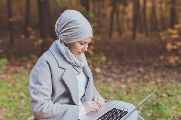 Mujer musulmana con su computadora portátil en el parque.