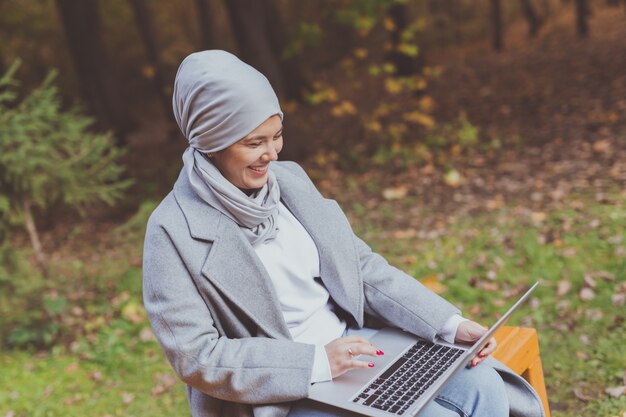 Mujer musulmana con su computadora portátil en el parque.