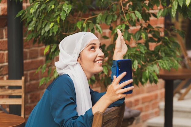 Mujer musulmana tomando selfie. Feliz hermosa niña con bufanda tomar una foto de sí misma usando el teléfono inteligente.