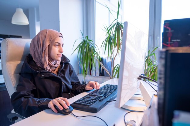 Mujer musulmana trabajando en una oficina usando una computadora con fondo blanco representa el poder de la mujer árabe
