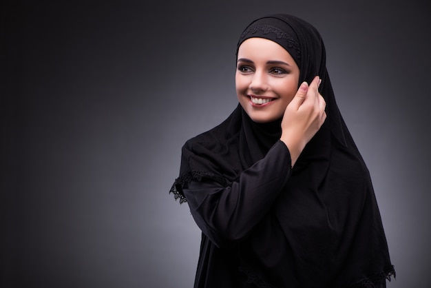 Mujer musulmana en vestido negro sobre fondo oscuro