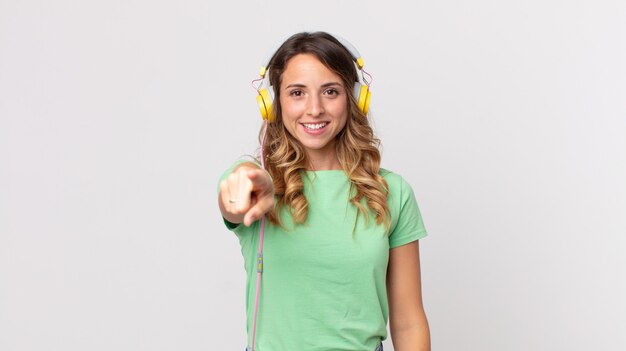 Mujer muy delgada apuntando a la cámara eligiéndote escuchando música con auriculares