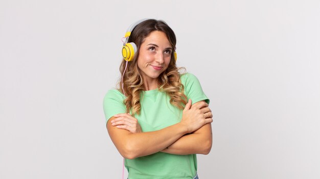 Mujer muy delgada encogiéndose de hombros, sintiéndose confundida e incierta escuchando música con auriculares