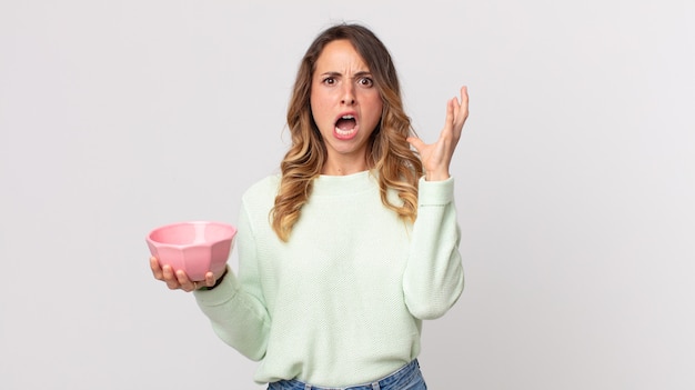 Mujer muy delgada gritando con las manos en el aire y sosteniendo una olla vacía