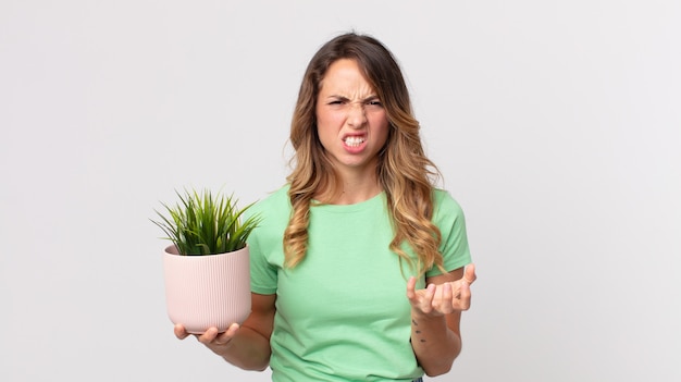 Mujer muy delgada que parece enojada, molesta y frustrada y sosteniendo una planta decorativa