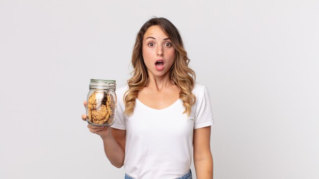 Mujer muy delgada que parece muy conmocionada o sorprendida y sosteniendo una botella de vidrio de galletas