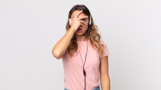 Mujer muy delgada que parece sorprendida, asustada o aterrorizada, cubriendo la cara con la mano. Asistente del operador con un auricular