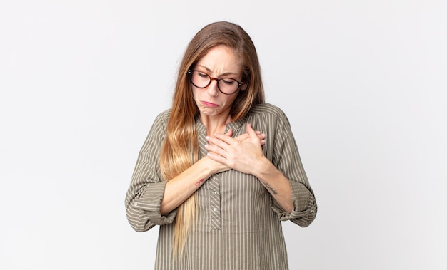 Mujer muy delgada que parece triste, herida y con el corazón roto, sosteniendo ambas manos cerca del corazón, llorando y sintiéndose deprimida