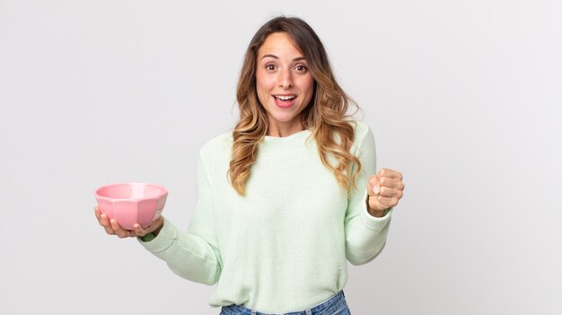 Mujer muy delgada que se siente conmocionada, riendo y celebrando el éxito y sosteniendo una olla vacía.