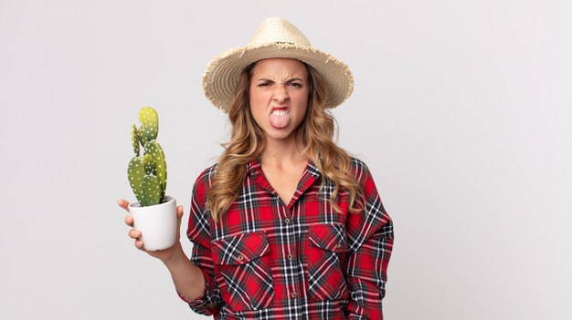 Mujer muy delgada que se siente disgustada e irritada y con la lengua fuera sosteniendo un cactus. concepto de granjero