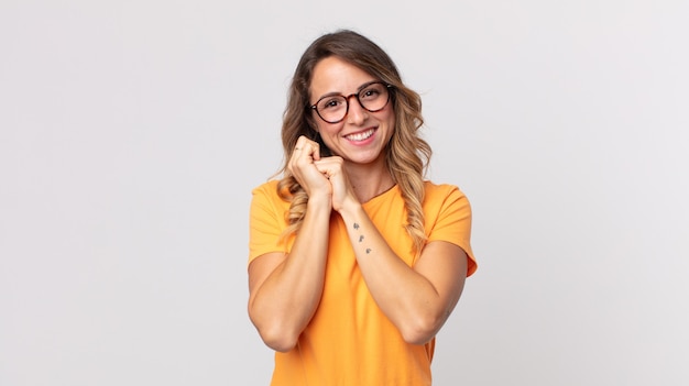 Mujer muy delgada que se siente enamorada y se ve linda, adorable y feliz, sonriendo románticamente con las manos al lado de la cara