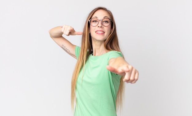 Mujer muy delgada que se siente feliz y segura, apuntando a la cámara con ambas manos y riendo, eligiéndote