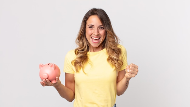 Mujer muy delgada que se siente sorprendida, riendo y celebrando el éxito y sosteniendo una alcancía