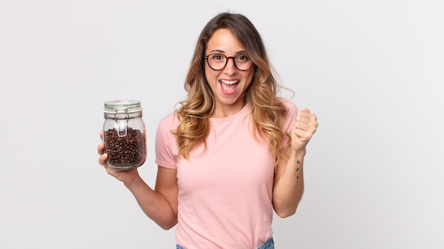 Mujer muy delgada que se siente sorprendida, riendo y celebrando el éxito y sosteniendo una botella de granos de café.