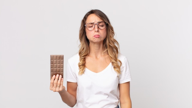 Mujer muy delgada que se siente triste y llorona con una mirada infeliz y llorando y sosteniendo una barra de chocolate